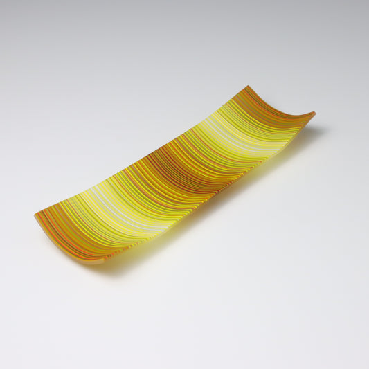A rectangular ColourWave fused glass plate, boasting vibrant vertical stripes in shades of yellow, orange, and green. The plate’s design features a gentle upward curve at each corner, giving it a subtle, shallow vessel shape suitable for artistic display.