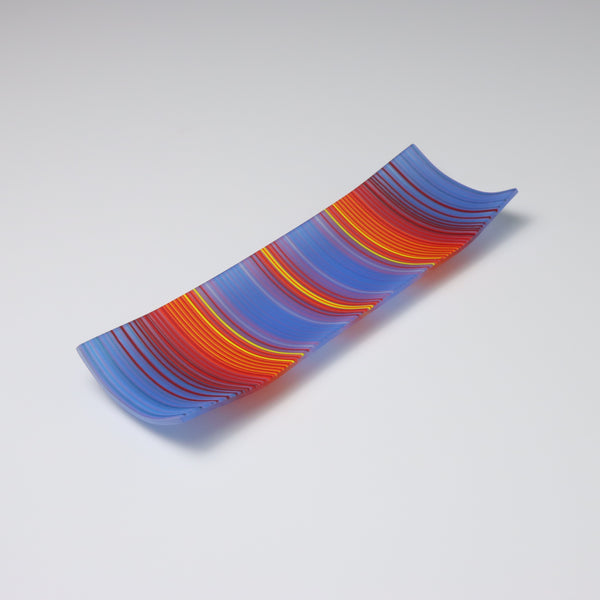 A rectangular ColourWave Glass fused glass plate showcasing a rich array of colours. The deep blues transition seamlessly into vibrant reds and yellows, creating a captivating visual effect. The plate is a testament to the artistic versatility of glass, serving as both a functional item and a piece of decorative art.