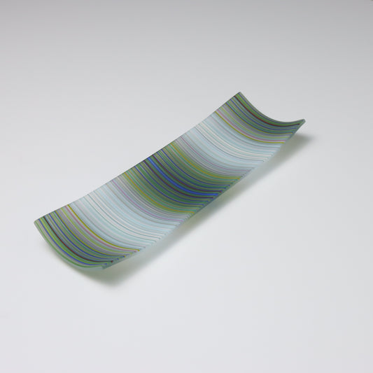 A handcrafted and kilnfired ColourWave Glass plate, rectangular with upturned corners creating a shallow bowl effect. The surface displays a beautiful wave pattern predominantly in grey and white, which upon closer inspection, is composed of a complex mix of many colours. The plate is set against a white background, emphasising its vibrant colours and artistic flair.