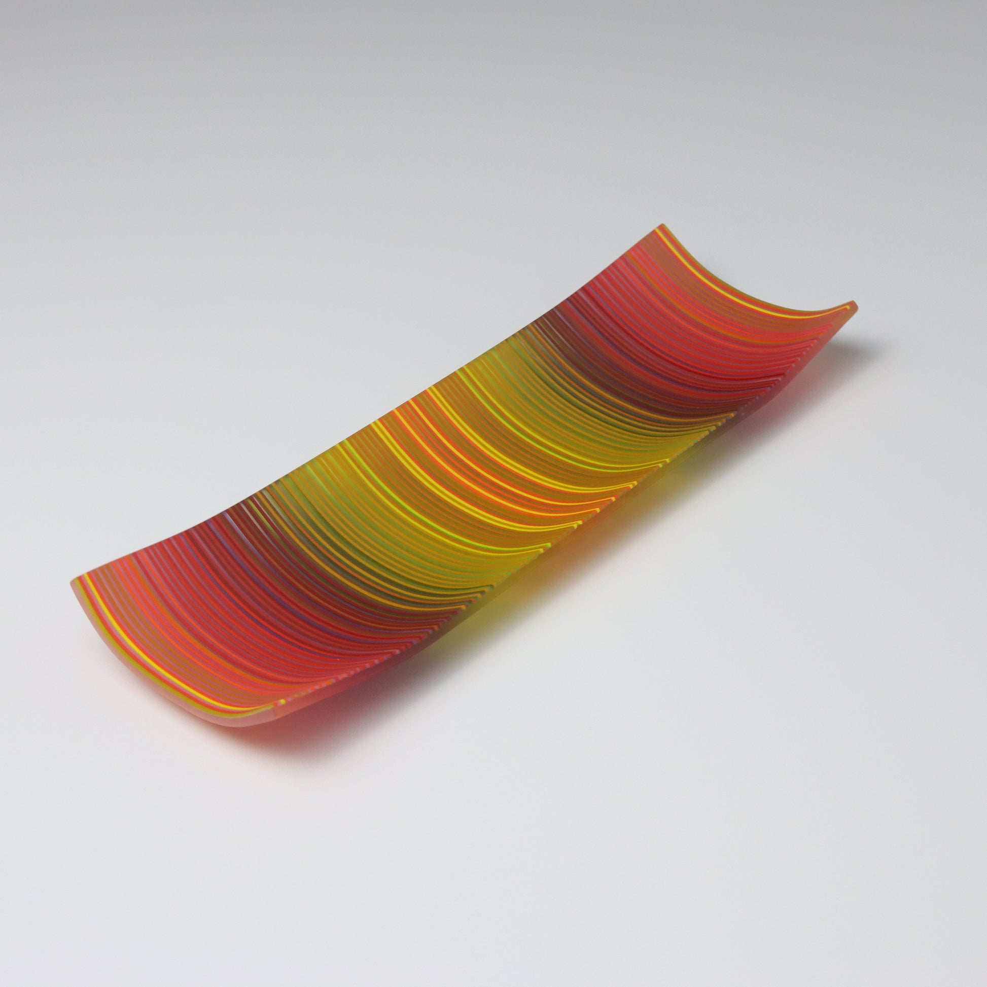 An enchanting ColourWave Glass fused glass plate, where the corners rise softly, framing a rich mosaic of autumn colours. Stripes of deep red, purple, green, and yellow, with a myriad of additional shades revealed upon close examination, create a visual celebration of autumn’s splendour.