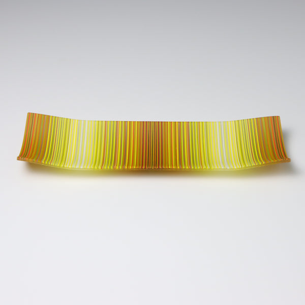 A rectangular ColourWave fused glass plate, boasting vibrant vertical stripes in shades of yellow, orange, and green. The plate’s design features a gentle upward curve at each corner, giving it a subtle, shallow vessel shape suitable for artistic display.