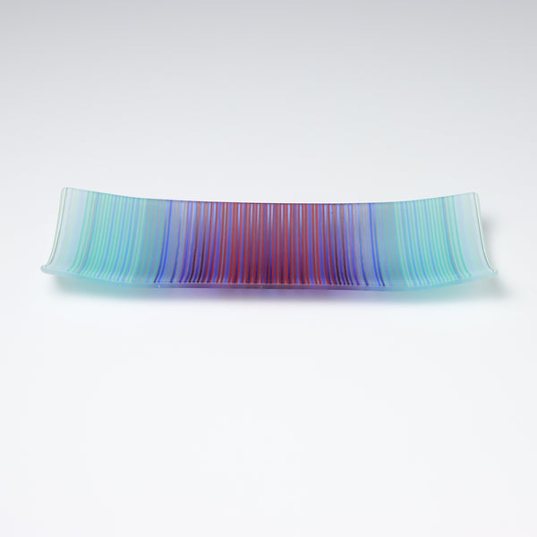 A rectangular ColourWave Glass fused glass plate, boasting a vibrant gradient from turquoise to deep blue and purple in vertical stripes. The plate’s corners elegantly curve upwards, adding a modern twist to its design. The smooth transition of colours offers a serene visual experience, while the craftsmanship reflects a high level of skill in glass work