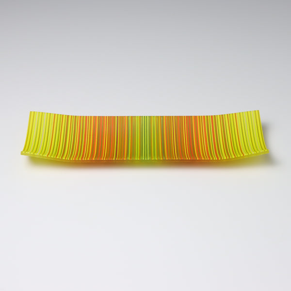 A ColourWave Glass fused glass plate, adorned with a vibrant pattern of vertical stripes in shades of yellow, green, orange, and red. The rectangular plate gently curves at the corners, forming a shallow bowl shape. The bright colours and sleek design emphasize its role as an attractive decorative piece.